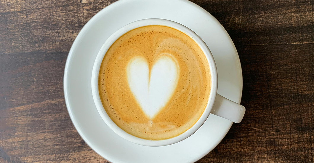 Tasse de café fumant vue de dessus avec un motif cœur en mousse de lait sur fond d'une table en bois brut