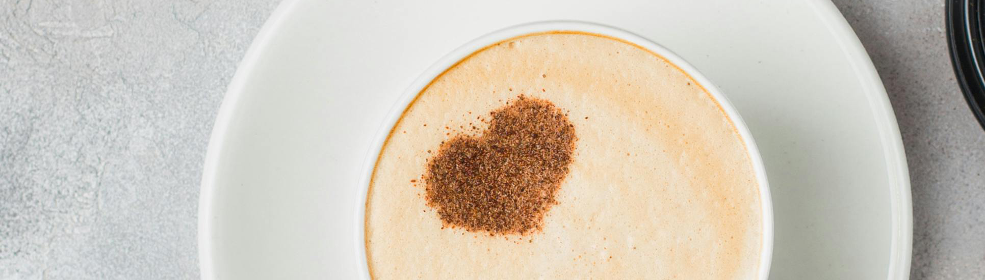 Tasse de café spécial avec un motif cœur en poudre de cacao, vue de dessus sur une soucoupe blanche.