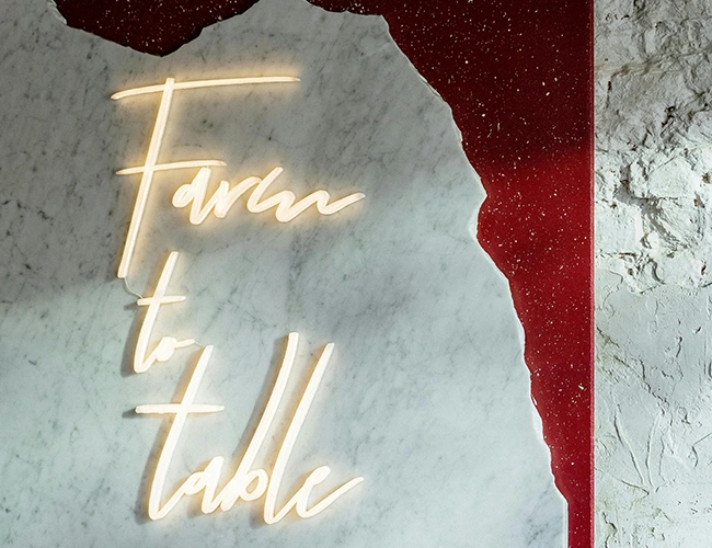 Enseigne lumineuse "Farm to table" sur un mur texturé, illustrant l'engagement du Bakery Bliss Café pour une cuisine locale, des produits frais et de saison.