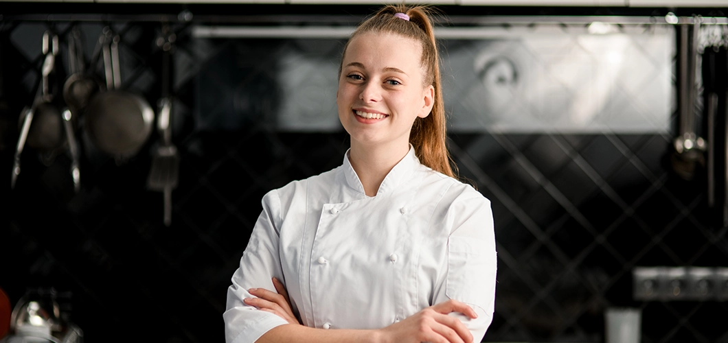Sophie, chef pâtissière du Bakery Bliss Café, souriante en tenue de cuisinière blanche dans la cuisine du coffee shop.