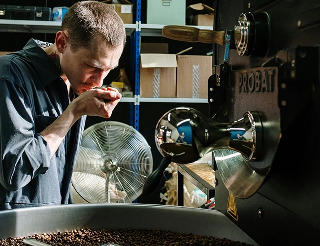 Torréfacteur de La Maison Deuza à Saint-Jean-de-Luz en train de sentir des grains de café fraîchement torréfiés à côté d'une machine Probat